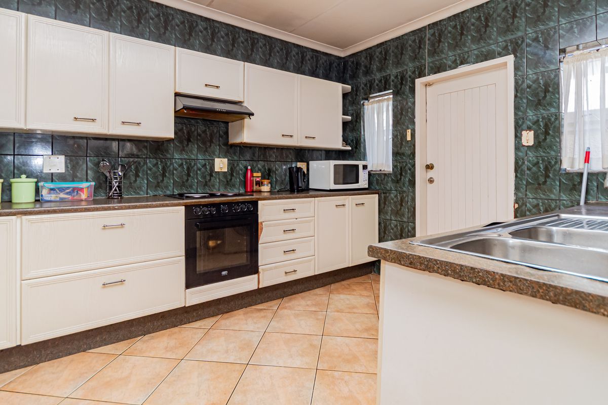 A functional kitchen featuring white cabinetry, dark tiled splashbacks, built-in oven with hob, and a double bowl sink with tiled flooring.