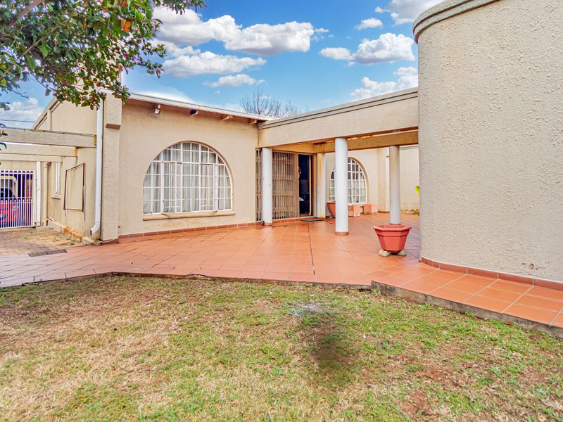 A spacious covered patio area featuring arched windows, tiled flooring, and structural columns, offering a functional outdoor space for relaxation.