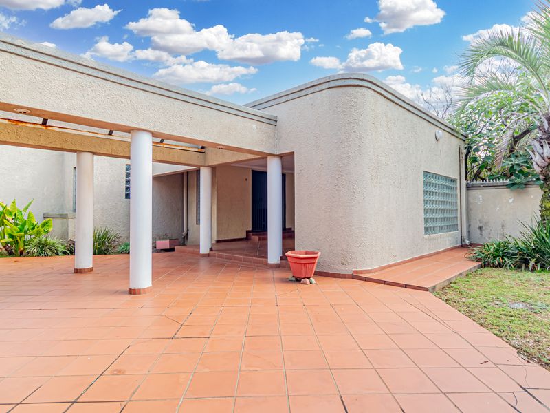 Front entrance area featuring a covered tiled patio with structural columns and a distinctive curved stucco facade with glass block detailing.