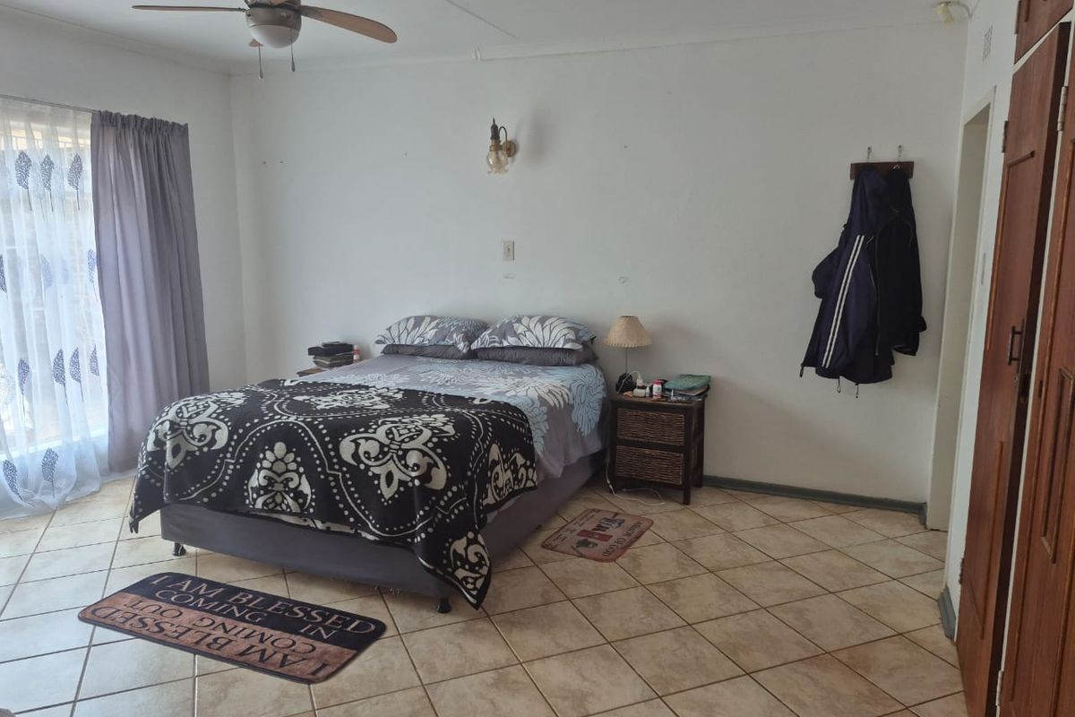 A spacious bedroom featuring tiled flooring, a ceiling fan, and built-in wooden cupboards, offering a functional and comfortable living space.