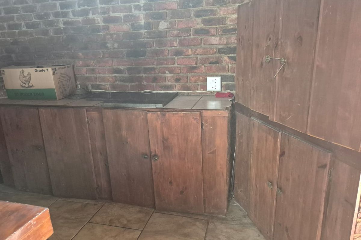 A rustic kitchen area featuring dark wood cabinetry, tiled countertops, and an exposed brick wall finish.