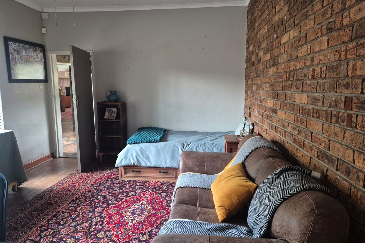 A bedroom featuring an exposed brick feature wall, laminate flooring, and a ceiling fan, offering a rustic aesthetic.
