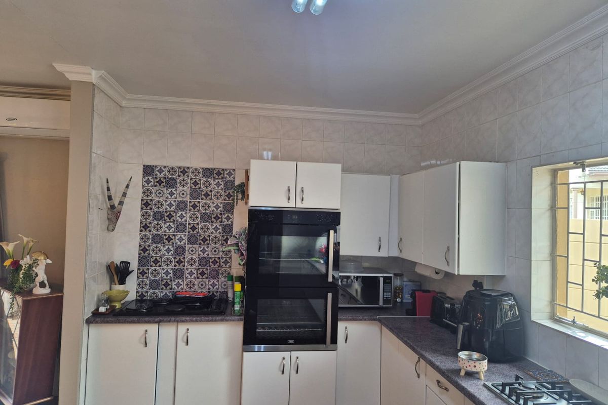 A functional kitchen featuring built-in double ovens, a gas hob, granite countertops, and decorative tiled splashbacks with ample cabinetry for storage.