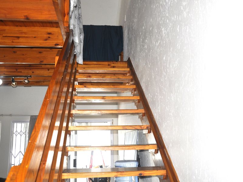 A timber staircase with matching balustrade leading to an upper level, featuring exposed timber ceiling beams and a view towards the entrance.