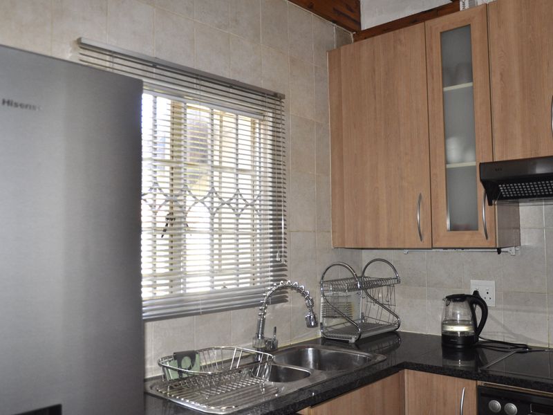 A functional kitchen featuring laminate cabinetry, granite countertops, a stainless steel double sink with a gooseneck faucet, and a tiled backsplash.