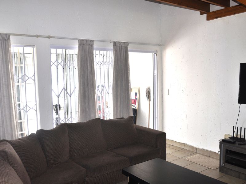 A living room featuring tiled flooring, exposed timber ceiling beams, and sliding glass doors with security gates leading to an outdoor area.