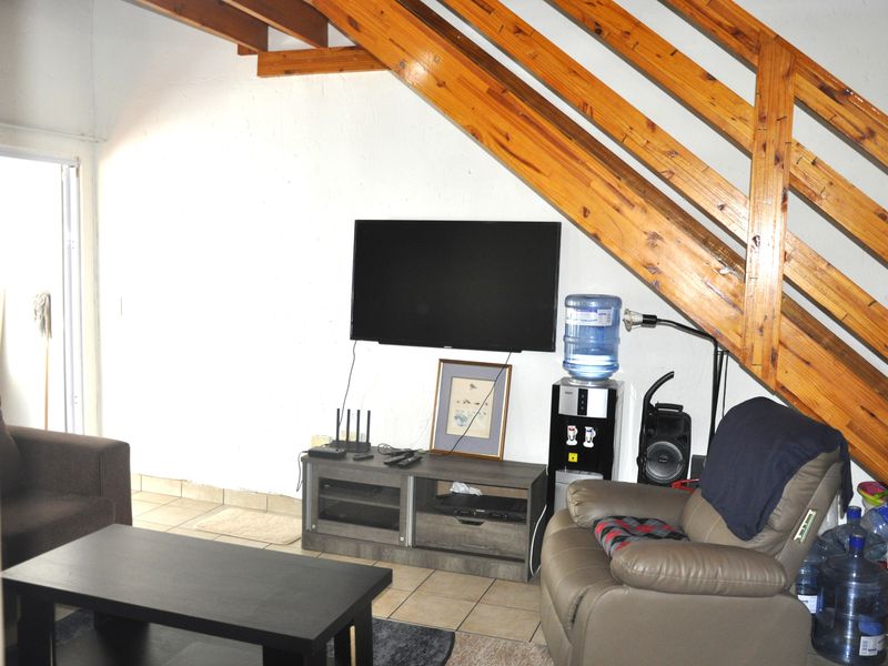 Living area featuring tiled flooring and a wooden staircase, providing a functional space under the stairs.