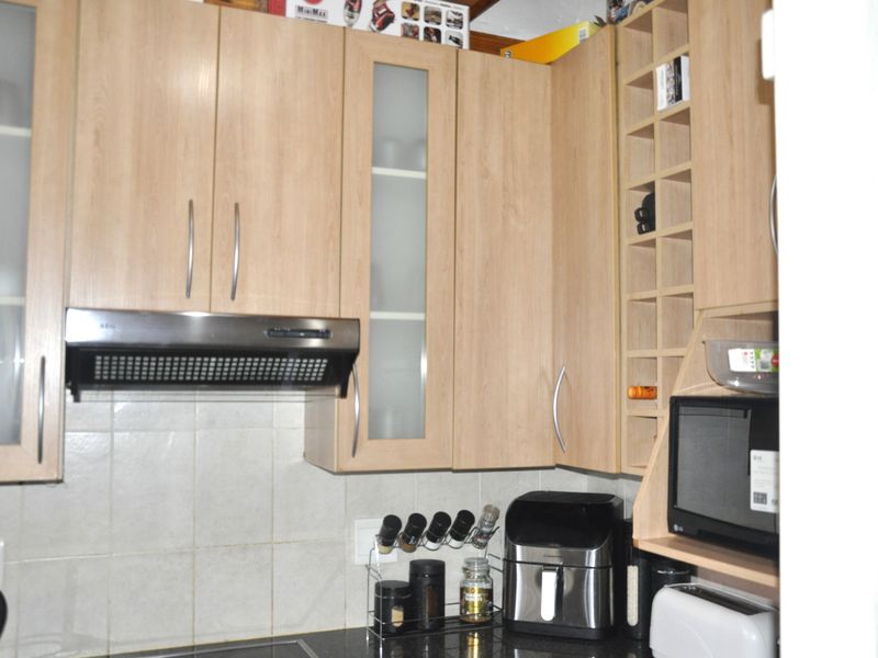 A functional kitchen featuring light wood-finish cabinetry, a tiled backsplash, integrated extractor fan, and dedicated wine storage rack.
