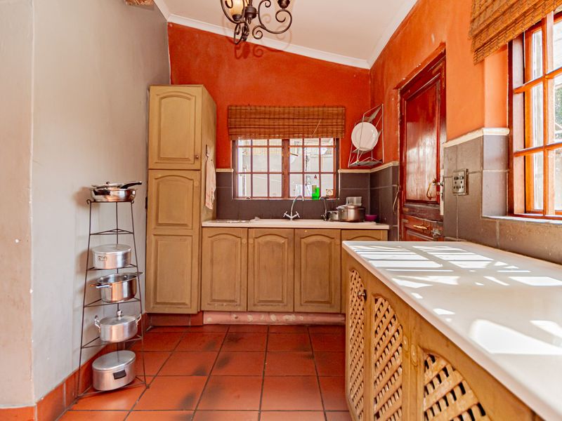 A dated kitchen featuring terracotta tiled flooring, built-in wooden cabinetry, and a tiled backsplash with natural light from timber-framed windows.
