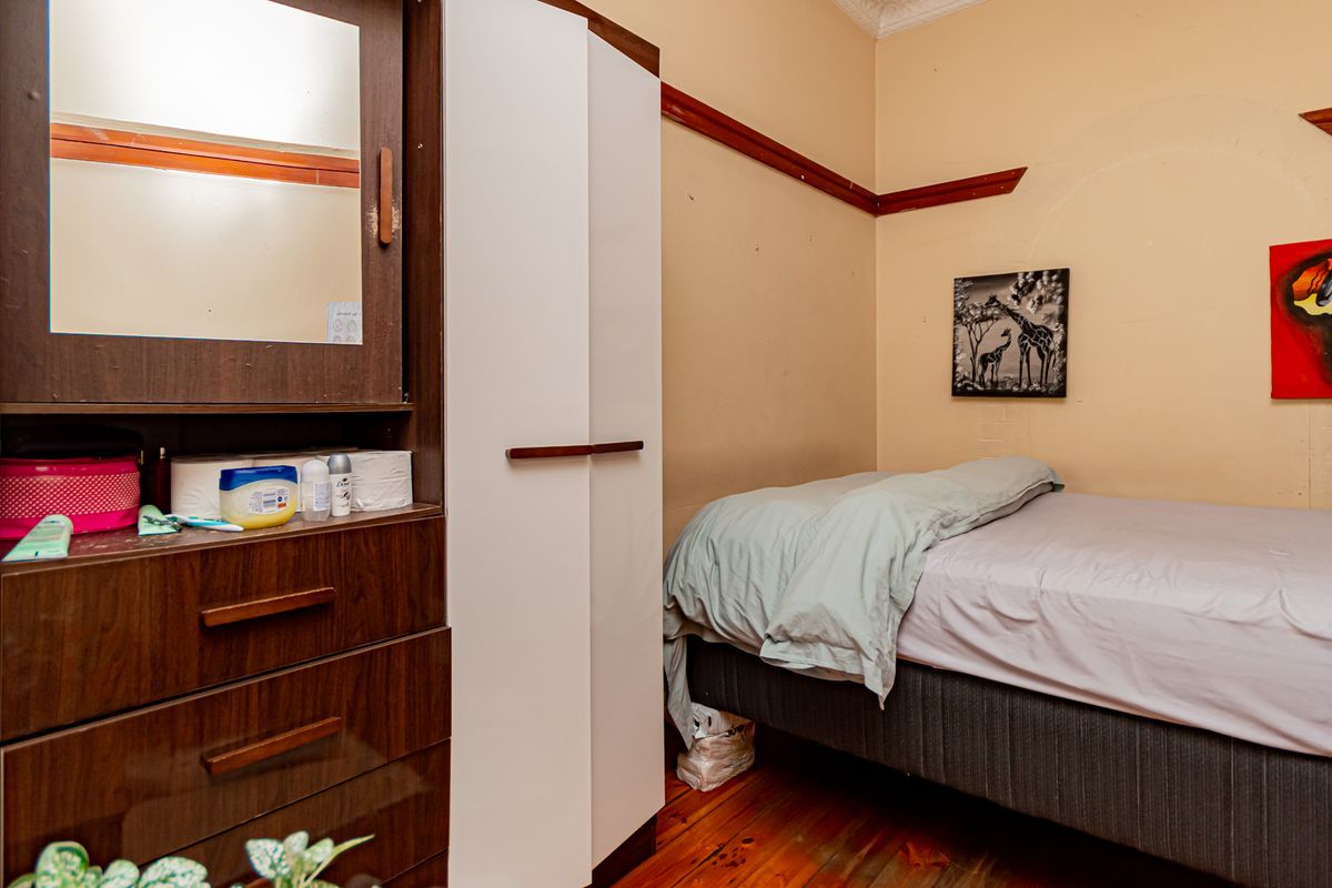 A bedroom featuring timber flooring, a built-in wardrobe, and a classic picture rail, offering a functional space with potential for cosmetic updates.