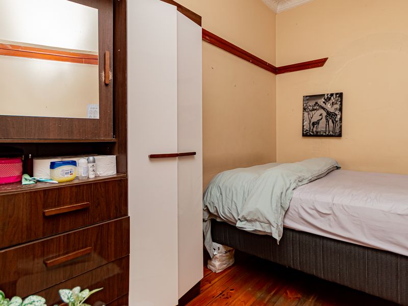 A bedroom featuring timber flooring, a built-in wardrobe, and a classic picture rail, offering a functional space with potential for cosmetic updates.