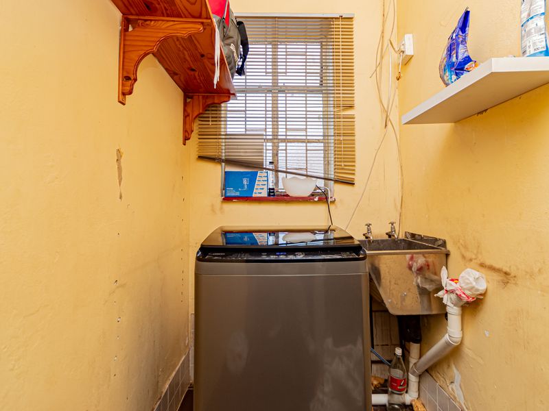 A functional laundry area featuring a stainless steel utility sink, wall-mounted shelving, and dedicated plumbing connections for a washing machine.