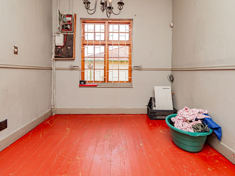 A utility space featuring timber flooring, a window with security bars, and an exposed electrical distribution board on the wall.