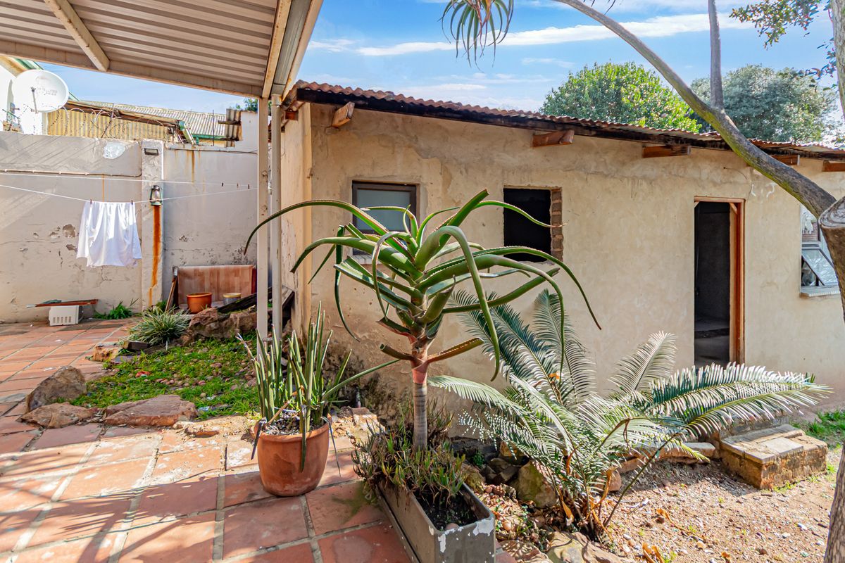 Rear exterior view featuring a covered patio area with terracotta tiling and a secondary structure requiring maintenance and cosmetic updates.