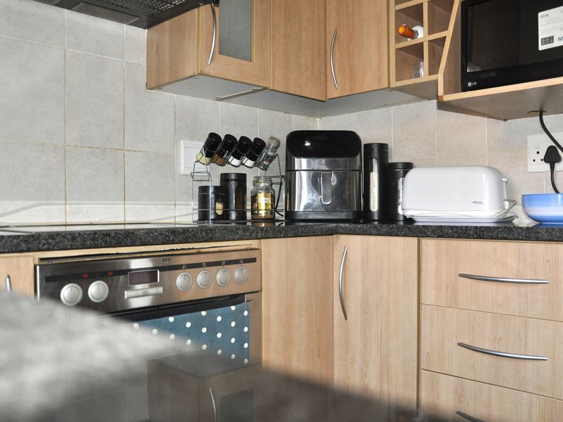 A functional kitchen featuring light wood-finish cabinetry, granite countertops, a built-in oven with hob, and a tiled backsplash.