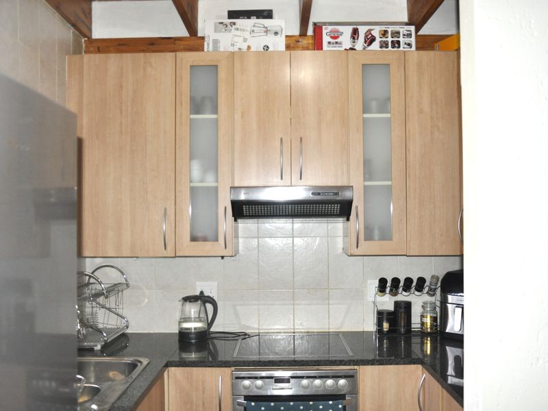 Compact kitchen featuring light wood-finish cabinetry, granite countertops, a tiled backsplash, and integrated stainless steel appliances.
