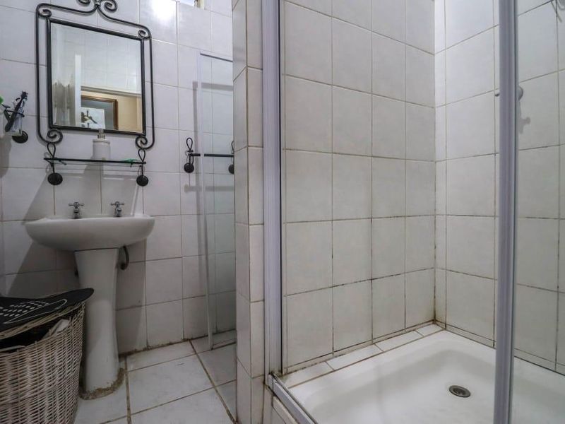 A functional bathroom featuring a pedestal basin and a shower enclosure with tiled walls and flooring, showing signs of wear in the grout.