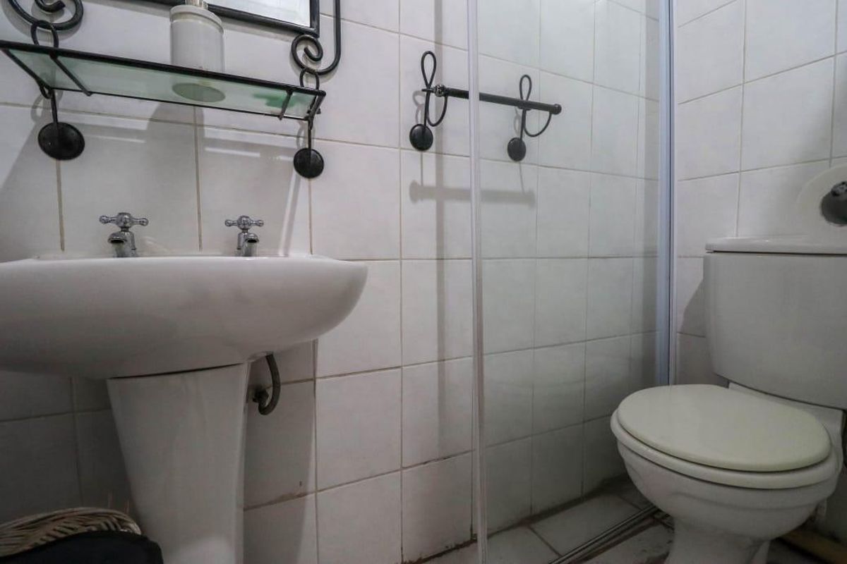 Compact bathroom featuring a pedestal basin, shower enclosure, and toilet with white ceramic wall tiling throughout.