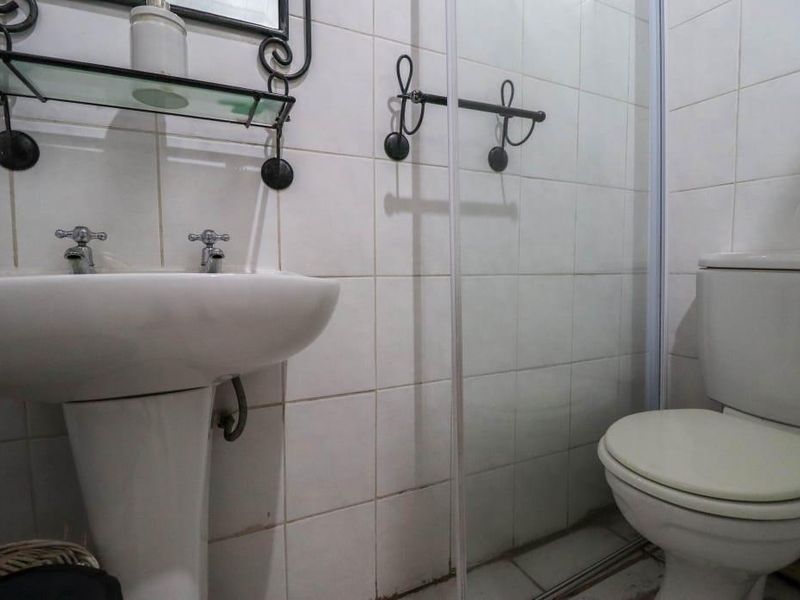 Compact bathroom featuring a pedestal basin, shower enclosure, and toilet with white ceramic wall tiling throughout.