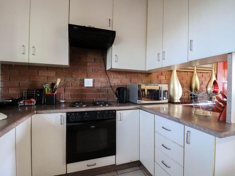 A functional kitchen featuring white cabinetry, laminate countertops, an integrated oven and hob, and a distinctive exposed brick backsplash.