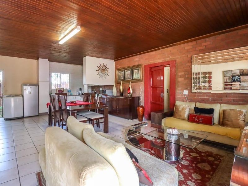 Spacious open-plan living and dining area featuring exposed brick walls, timber ceiling, and tiled flooring, offering a functional layout for family living.
