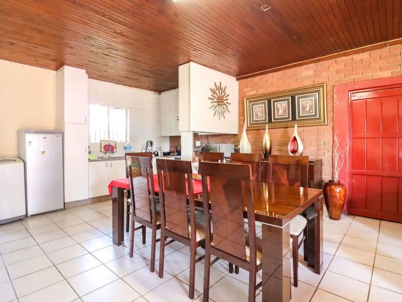 Open plan dining and kitchen area featuring exposed brick walls, timber ceiling, and tiled flooring, offering a functional layout with potential for modern updates.