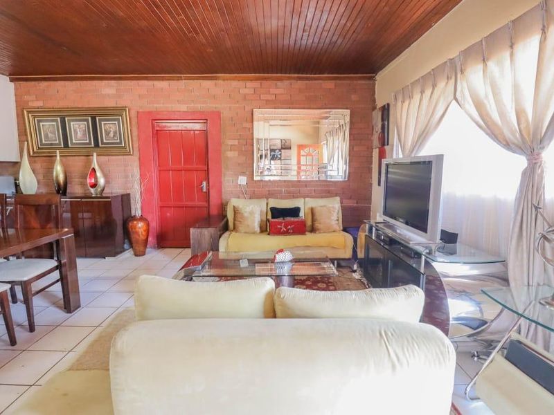 Open plan living and dining area featuring exposed brick walls, timber panelled ceilings, and tiled flooring in a cottage-style home.