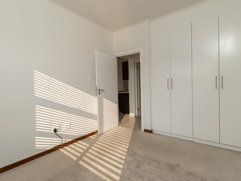 A bright, empty bedroom featuring neutral carpeting and ample built-in cupboard storage, with a doorway leading to an adjacent room.