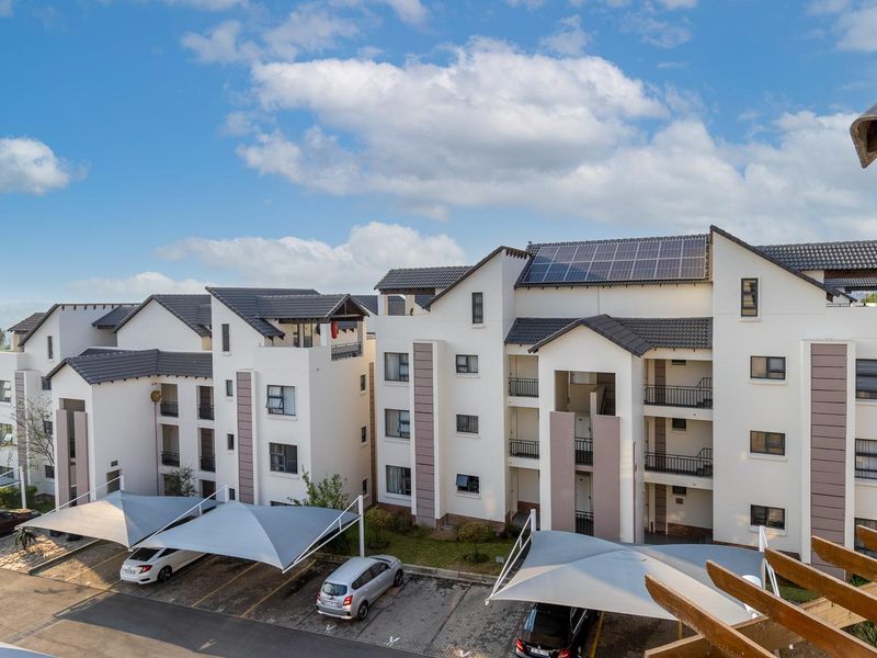An elevated view of a modern apartment complex featuring white facades, tiled roofs with solar panels, and designated covered parking areas.