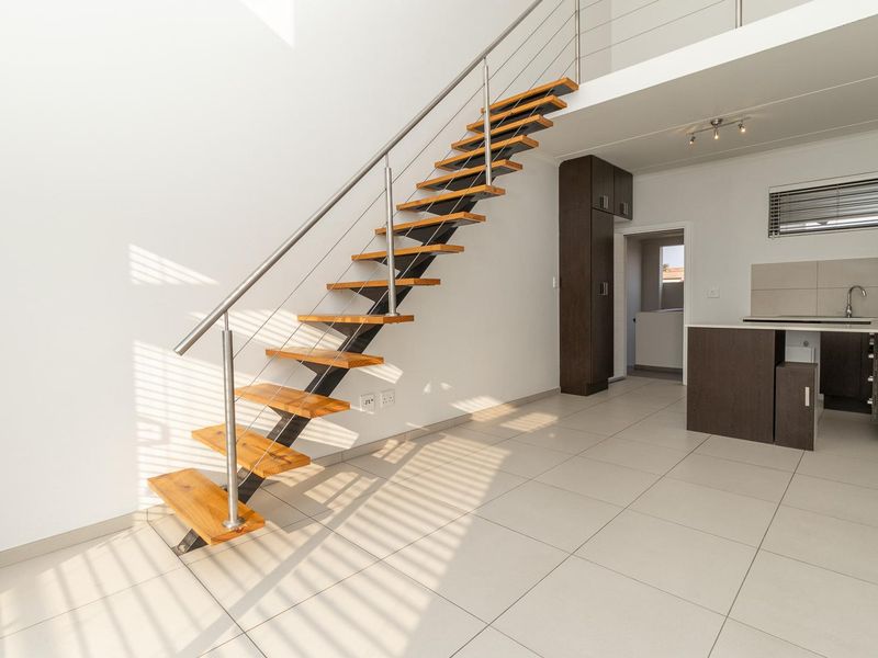 Modern open-plan living area featuring a striking timber staircase with stainless steel balustrade, tiled flooring, and a compact, functional kitchen space.