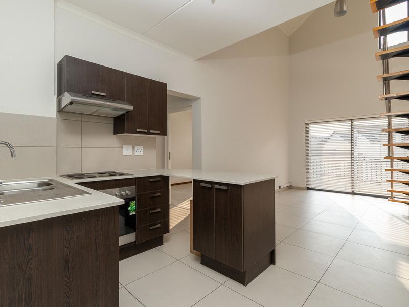 Open-plan kitchen and living area featuring dark wood cabinetry, tiled floors, and a modern spiral staircase leading to an upper level.