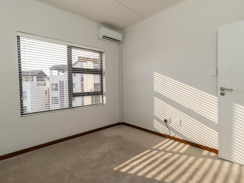 A clean, empty bedroom featuring neutral carpeting, an installed air conditioning unit, and venetian blinds on the window.