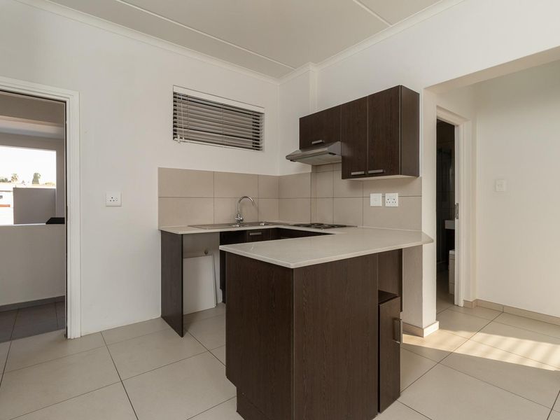 A clean, modern kitchen featuring dark wood cabinetry, stone countertops, a built-in extractor fan, and neutral tiled flooring.