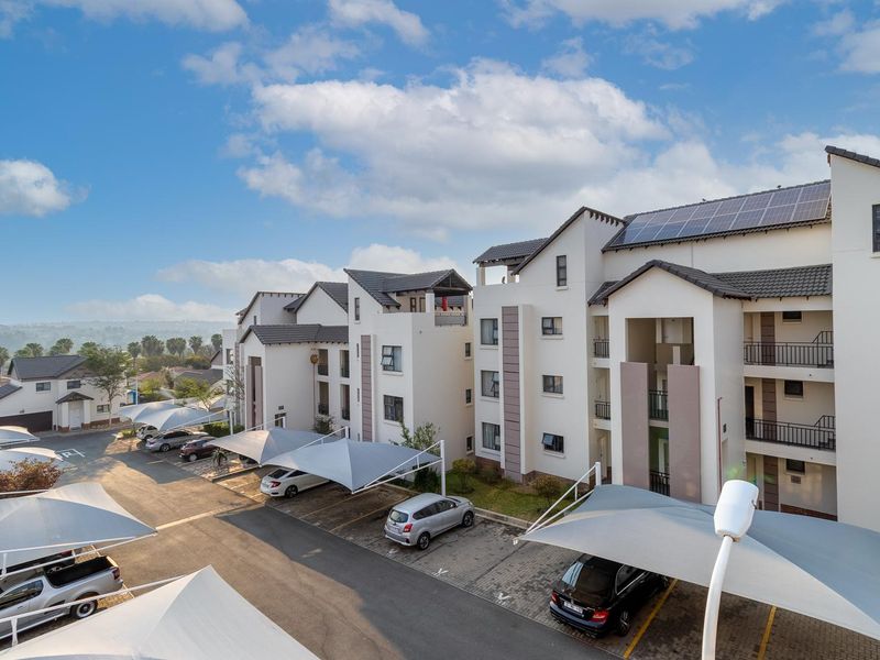 Exterior view of a modern apartment complex featuring paved parking areas with shade sails, balconies, and roof-mounted solar panels.