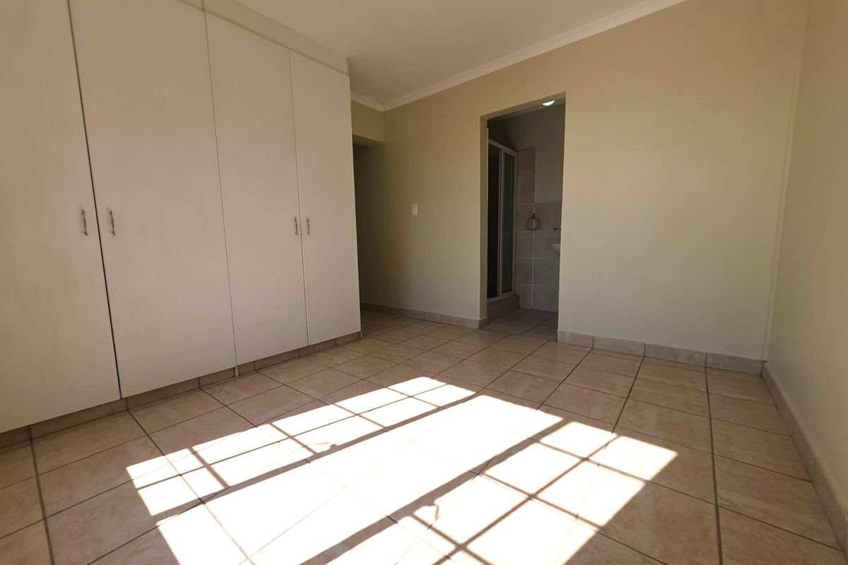 A bright, empty bedroom featuring built-in cupboards, tiled flooring, and direct access to an en-suite bathroom.
