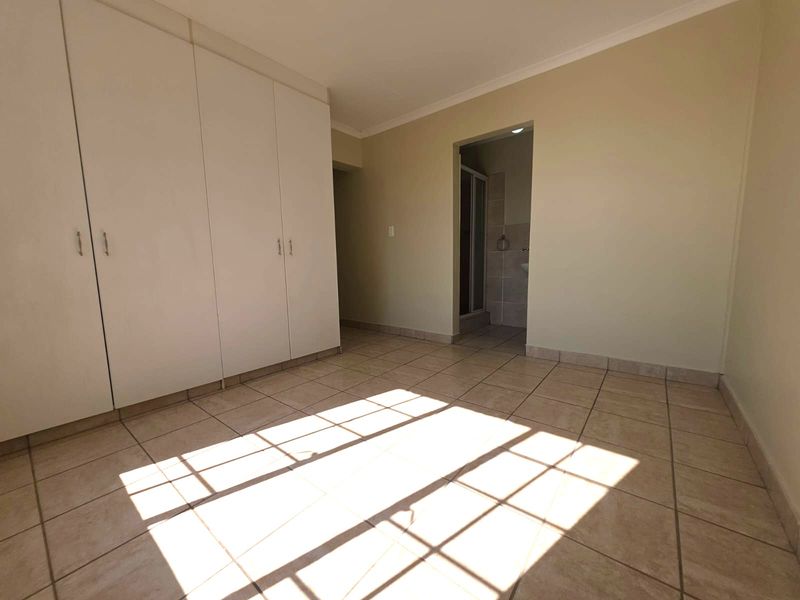 A bright, empty bedroom featuring built-in cupboards, tiled flooring, and direct access to an en-suite bathroom.