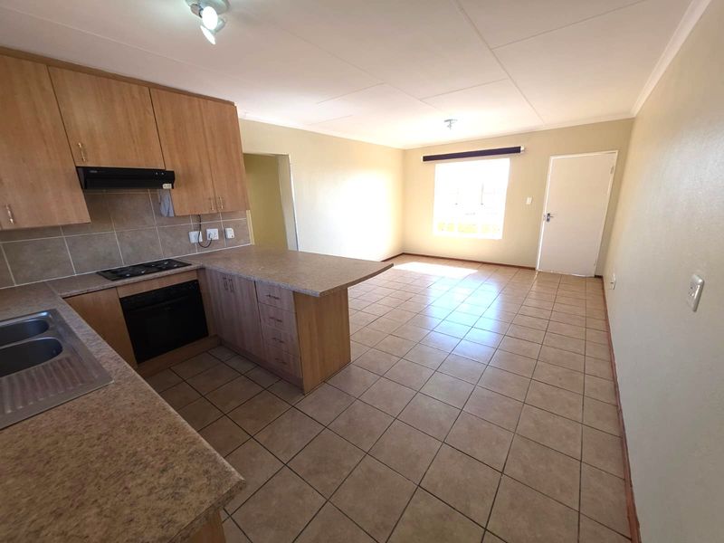 Open-plan living area featuring a functional kitchen with built-in cabinetry, oven, hob, and tiled flooring throughout the space.