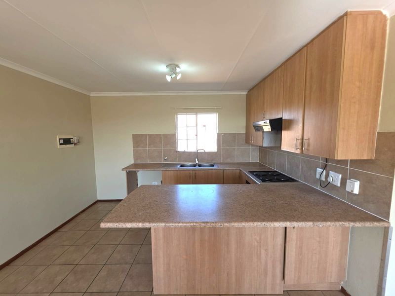 A functional kitchen featuring laminate cabinetry, a breakfast bar, electric hob with extractor fan, and tiled flooring in a neutral, open-plan layout.