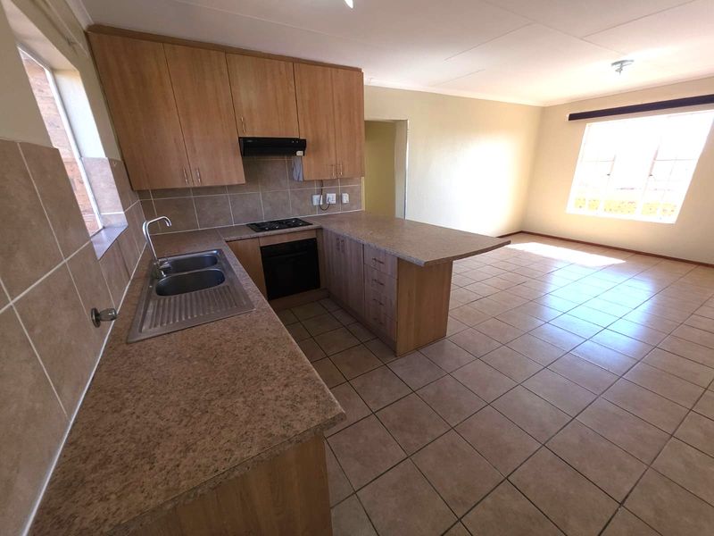 Open-plan kitchen and living area featuring laminate cabinetry, built-in appliances, tiled flooring, and ample natural light.