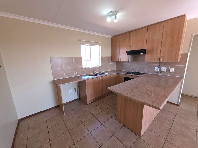 A functional, empty kitchen featuring laminate cabinetry, stone-look countertops, a built-in hob with extractor fan, and tiled flooring.