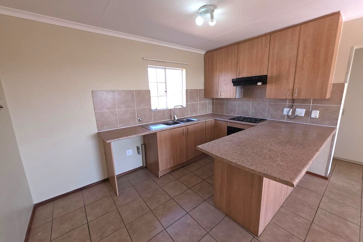 A functional, empty kitchen featuring laminate cabinetry, stone-look countertops, a built-in hob with extractor fan, and tiled flooring.