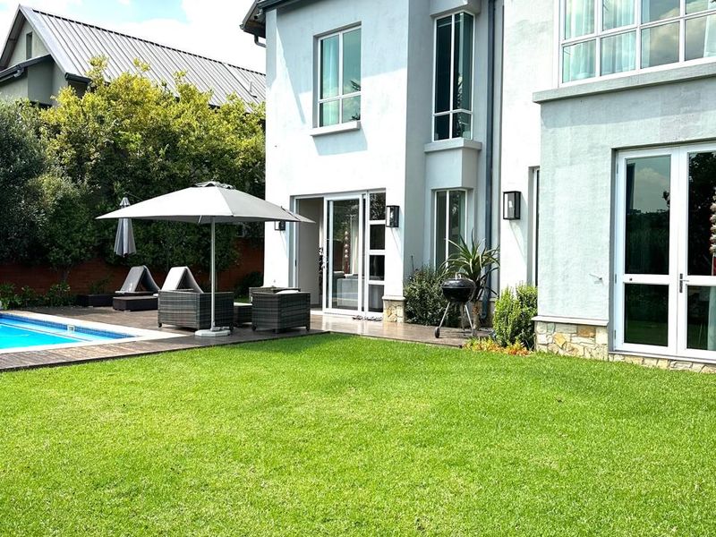 Rear view of a modern two-story house featuring a well-maintained lawn, swimming pool, and wooden decking area.
