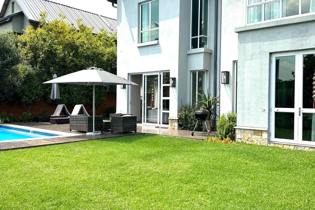 Rear view of a modern two-story house featuring a well-maintained lawn, swimming pool, and wooden decking area.