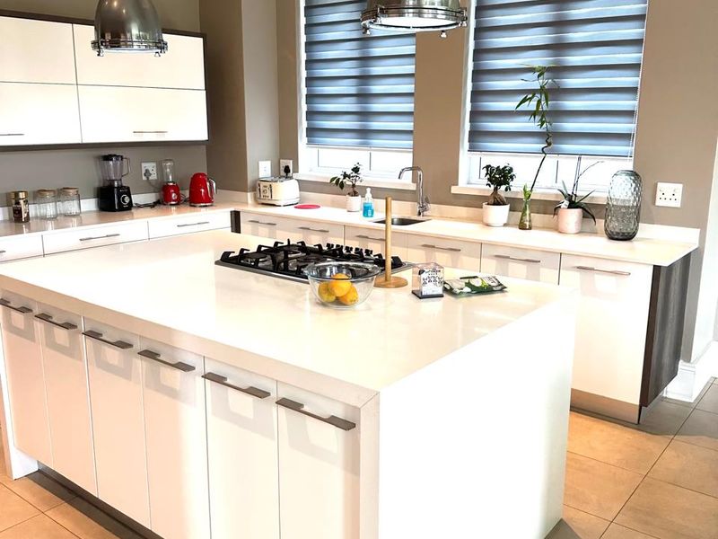 Modern kitchen featuring a large central island with a gas hob, stone countertops, sleek white cabinetry, and stylish pendant lighting.