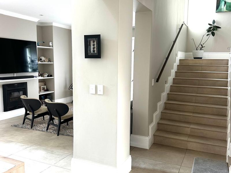 Open plan living area featuring a built-in fireplace, custom shelving, tiled flooring, and a staircase with a modern handrail.