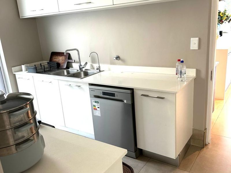 A clean and functional scullery featuring white cabinetry, stone countertops, a stainless steel sink, and an integrated dishwasher.