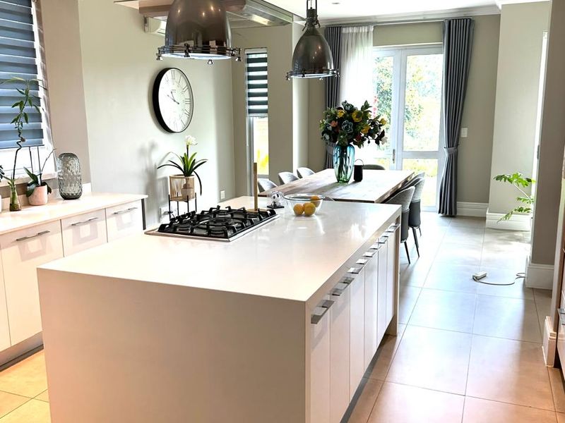 Modern open-plan kitchen and dining area featuring a large central island with gas cooktop, sleek cabinetry, and direct access to the outdoor space.