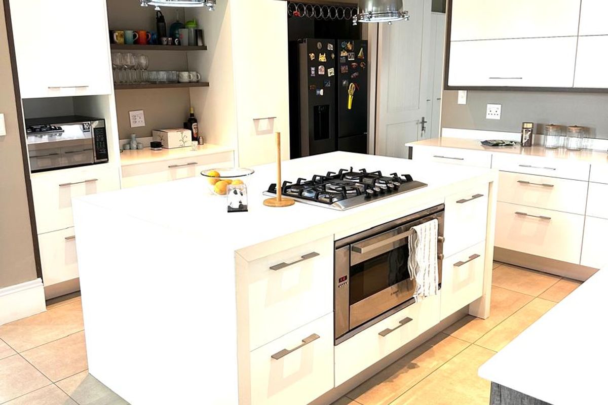 Modern kitchen featuring a central island with a built-in gas cooktop, oven, stainless steel extractor fan, and ample white cabinetry with tiled flooring.