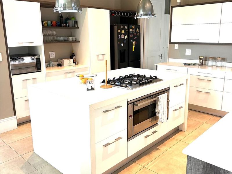 Modern kitchen featuring a central island with a built-in gas cooktop, oven, stainless steel extractor fan, and ample white cabinetry with tiled flooring.