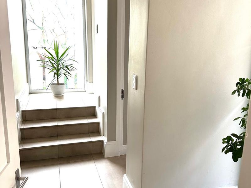 A bright and clean hallway featuring neutral tiled flooring, a small internal staircase, and a large window providing natural light.